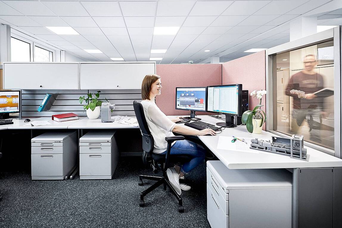 Mitarbeiterin arbeitet an einem Dual-Monitor-Arbeitsplatz in einem modernen, hell eingerichteten Büro.