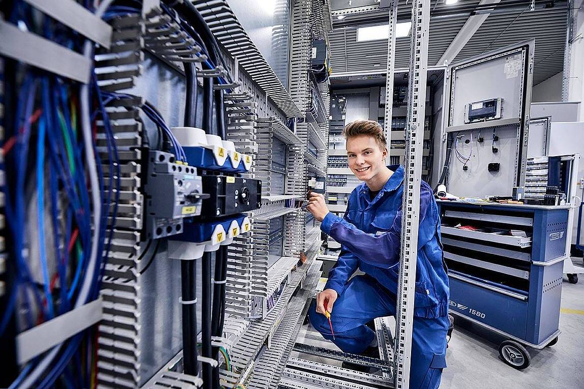 Ein junger Elektroniker für Betriebstechnik arbeitet an einem großen Schaltschrank.