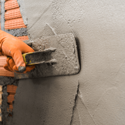 Eine Hand, die mit einem Spachtel eine Wand verputzt.